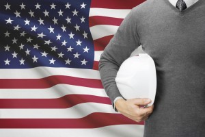 Man standing with hard hat in from of United States of America's flag. 