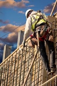 A construction worker on a high wall against colorful sunrise clouds.